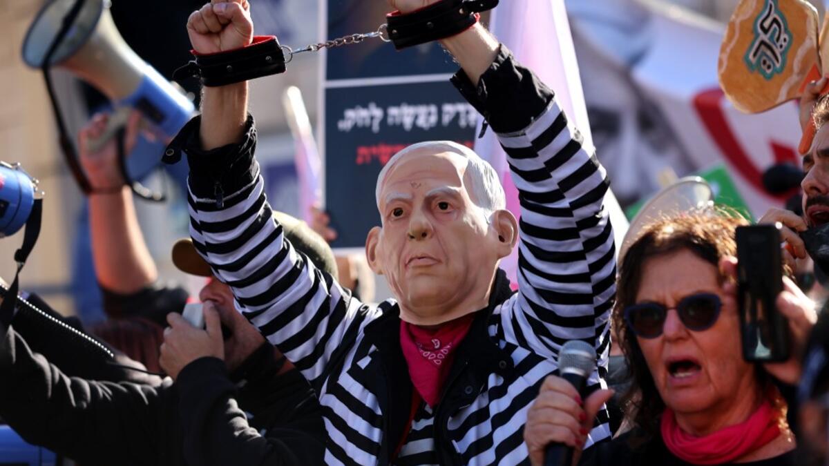 A demonstrator wearing a mask representing Prime Minister Benjamin Netanyahu gestures during a demonstration outside the court, as his corruption trial resumes in occupied east Jerusalem, on February 8, 2021. Israel's Prime Minister Benjamin Netanyahu returns to court to formally respond to the corruption charges against him, as his trial enters an intensified phase six weeks before he faces re-election. EMMANUEL DUNAND / AFP