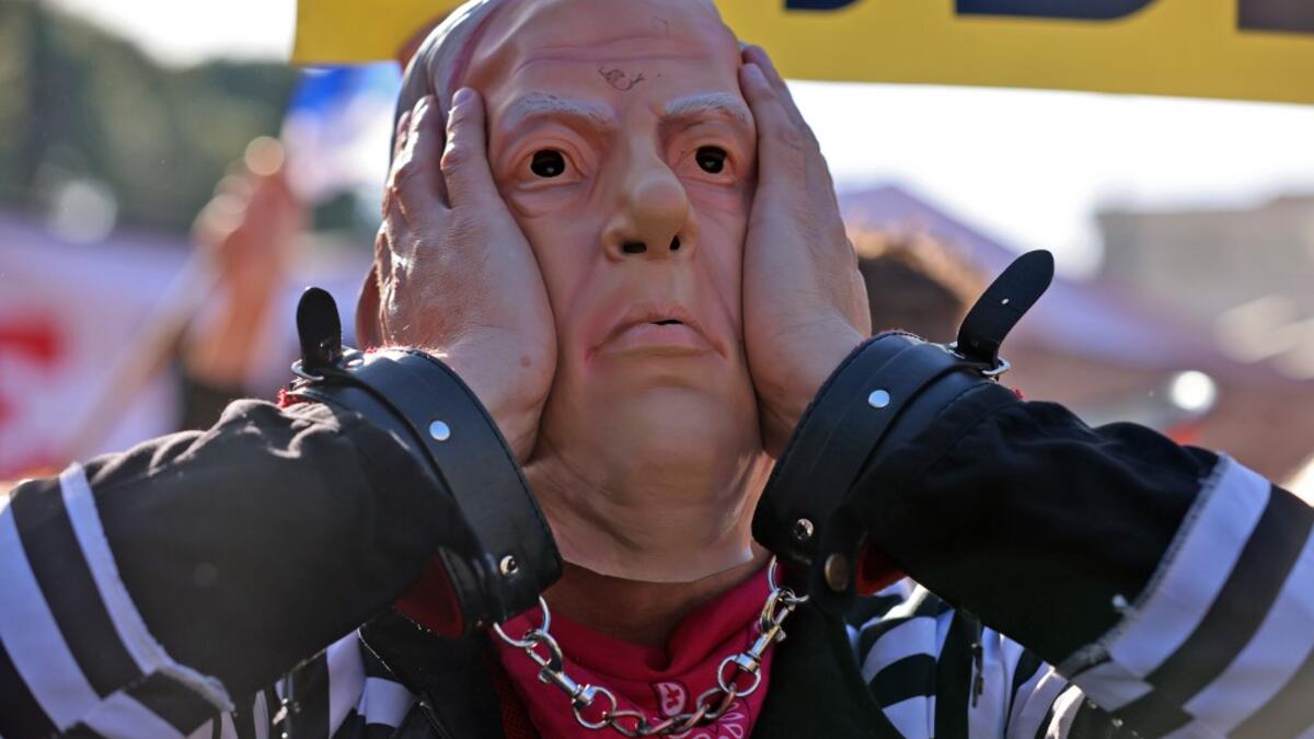 A demonstrator wearing a mask representing Prime Minister Benjamin Netanyahu gestures during a demonstration outside the court, as his corruption trial resumes in occupied east Jerusalem, on February 8, 2021. Israel's Prime Minister Benjamin Netanyahu returns to court to formally respond to the corruption charges against him, as his trial enters an intensified phase six weeks before he faces re-election. EMMANUEL DUNAND / AFP