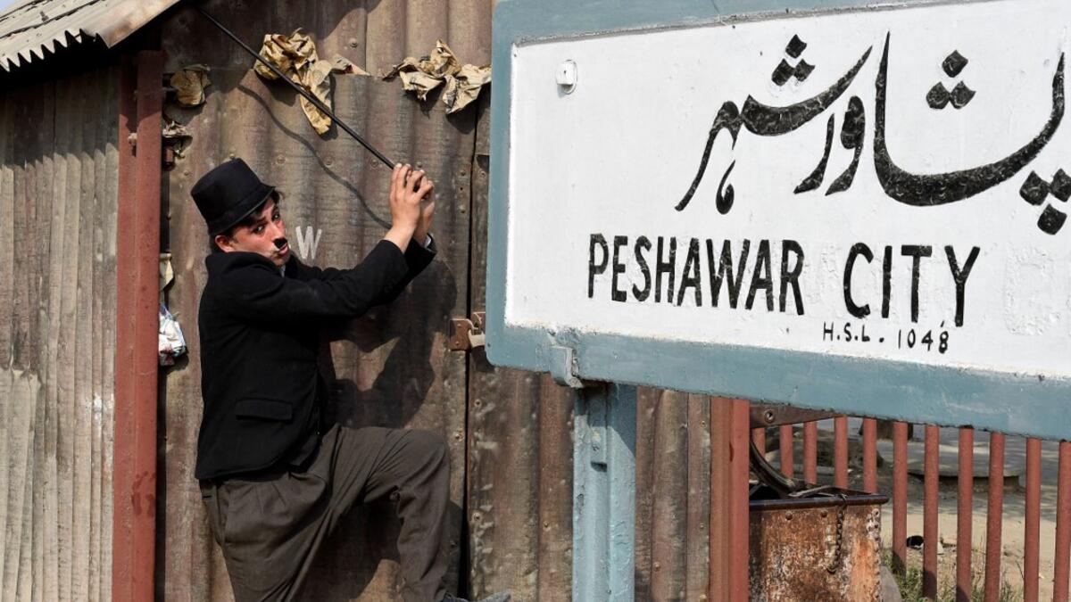 In this picture taken on February 9, 2021, street actor Usman Khan, dressed up as silent film star Charlie Chaplin, performs in the Pakistan's northwestern city of Peshawar. Wearing a bowler hat and familiar toothbrush moustache, Pakistan's Usman Khan darts through traffic swinging a cane, teasing motorists and shopkeepers for laughs and a few rupees with a Charlie Chaplin impersonation that has become a viral sensation.  Abdul MAJEED / AFP