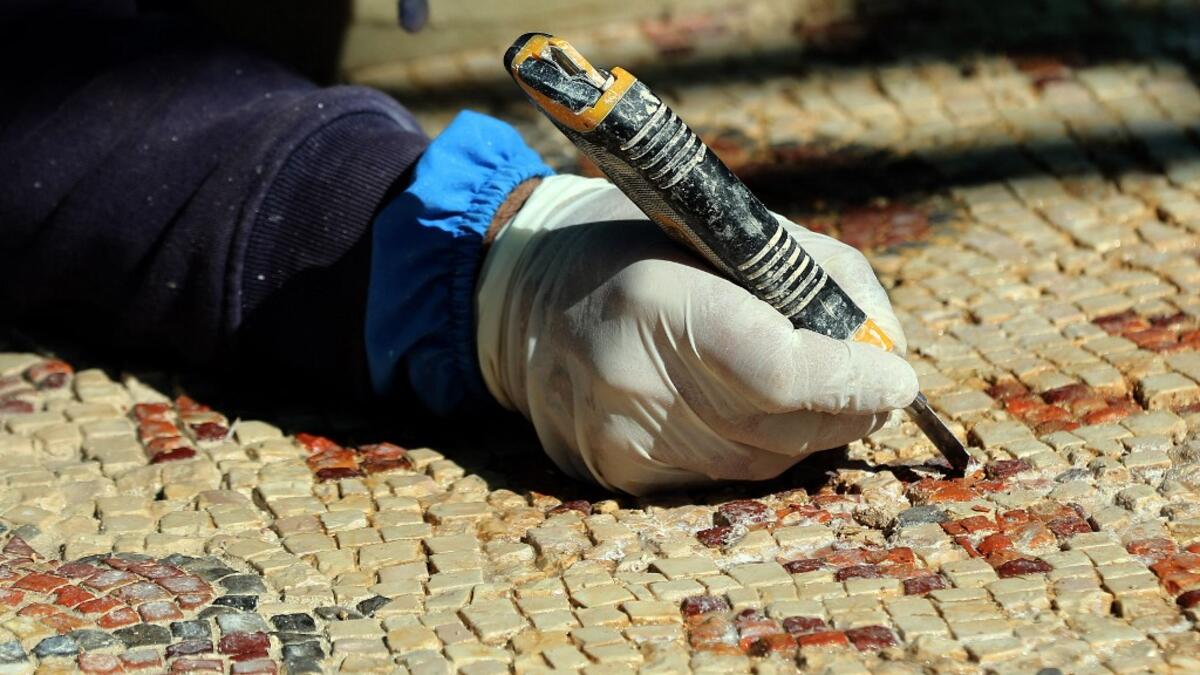 A worker employed by a pilot project run by the UN cultural agency UNESCO, restores a mosaic floor at an ancient church complex, in the small town of Rihab, some 70 kilometres north of the Jordanian capital Amman, on February 9, 2021. In the ruins of the ancient Byzantine church in Jordan, local townspeople and Syrian refugees work side by side on a project that unites preserving cultural heritage and fighting poverty.  Khalil MAZRAAWI / afp