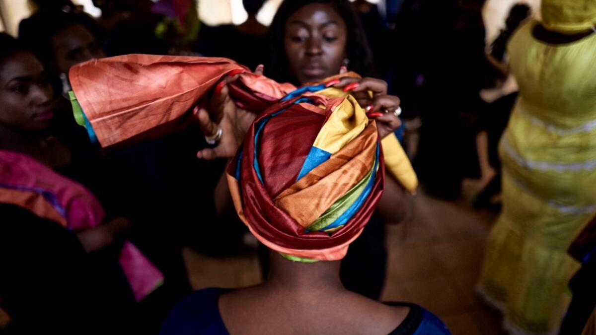 A dresser helps a gold miner to wear a turban in the backstage prior to take part in a fashion show as part of the first edition of the International Gold Fair Afrik'Or, in Bamako, on February 12, 2021. The Princess of Burundi Esther Kamatari, selected 34 women among gold mines workers in southern Mali, to walk down the catwalk for a fashion show organised during the International Gold Fair. Gold represents 15% of Mali's exports and more than 20% of its GDP estimated at nearly US$20 billion by the end of 20
