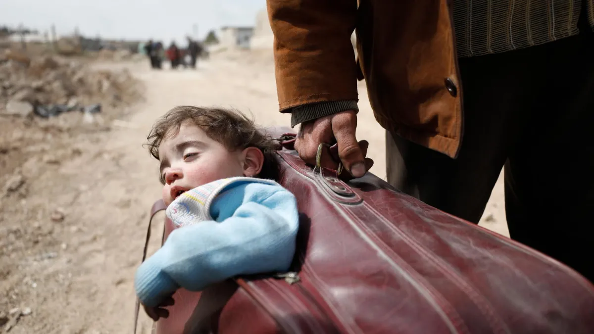 On 15 March 2018 in Beit Sawa, eastern Ghouta, a man carrying a child in a suitcase walks towards Hamourieh where an evacuation exit from eastern Ghouta has been opened.