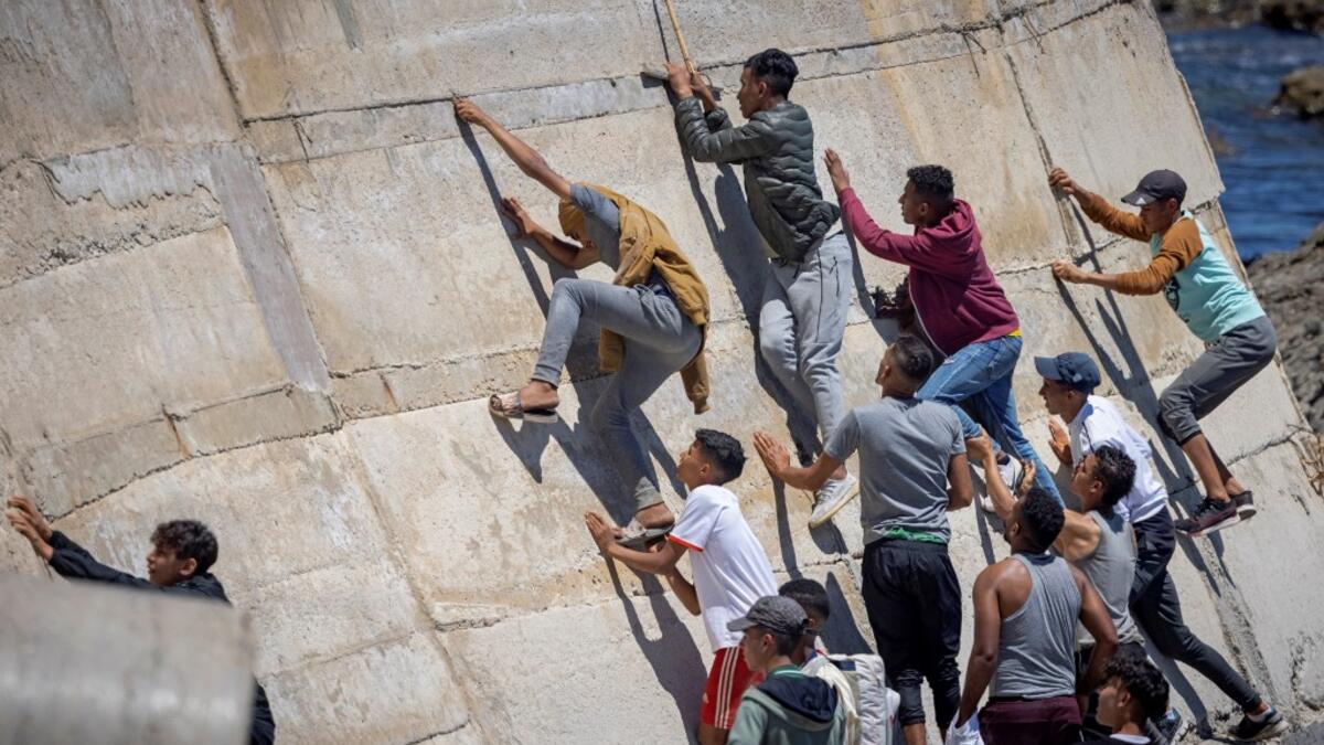 Migants climb a sea wall in the northern town of Fnideq after attempting to cross the border from Morocco to Spain's North African enclave of Ceuta on May 19, 2021. Spain stepped up diplomatic pressure on Rabat as its prime minister flew into Ceuta, vowing to "restore order" in the North African enclave after a record 8,000 migrants reached its beaches from Morocco