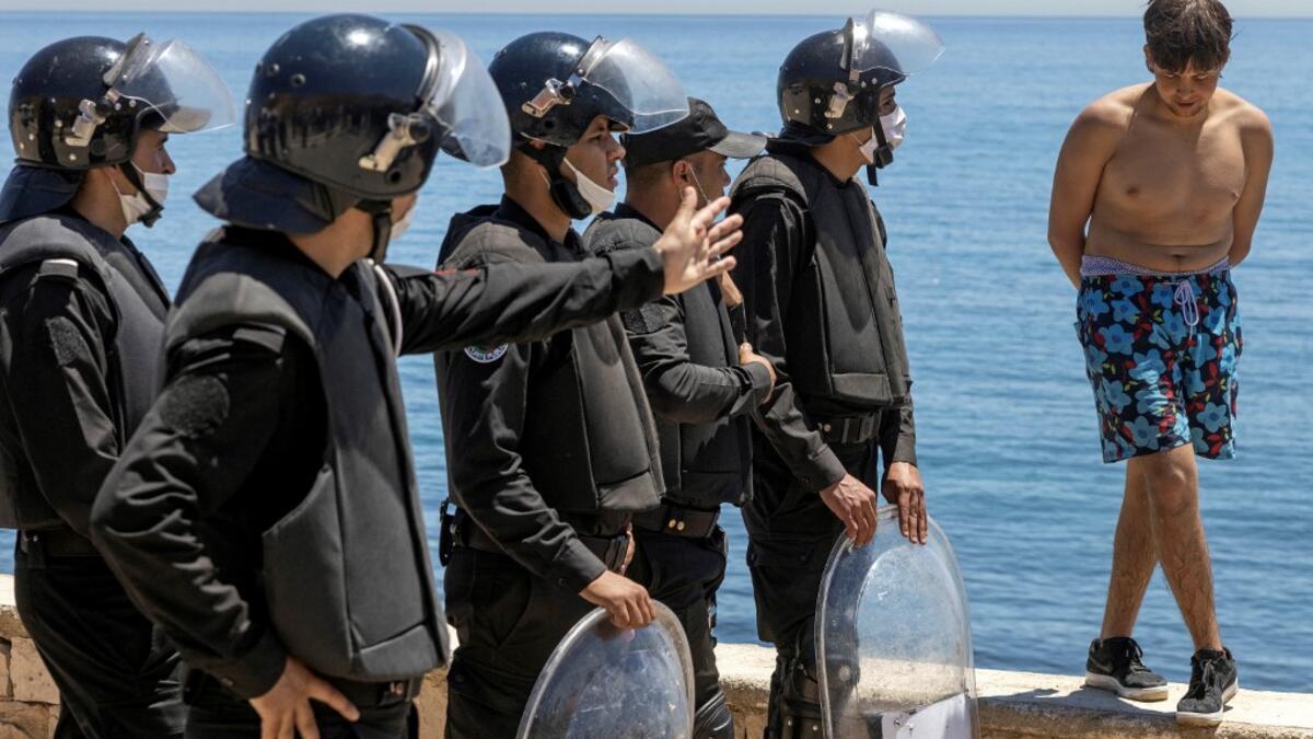 Moroccan police speak to a migrant as he stands on a sea wall in the northern town of Fnideq after attempting to cross the border from Morocco to Spain's North African enclave of Ceuta on May 19, 2021. Spain stepped up diplomatic pressure on Rabat as its prime minister flew into Ceuta, vowing to "restore order" in the North African enclave after a record 8,000 migrants reached its beaches from Morocco.