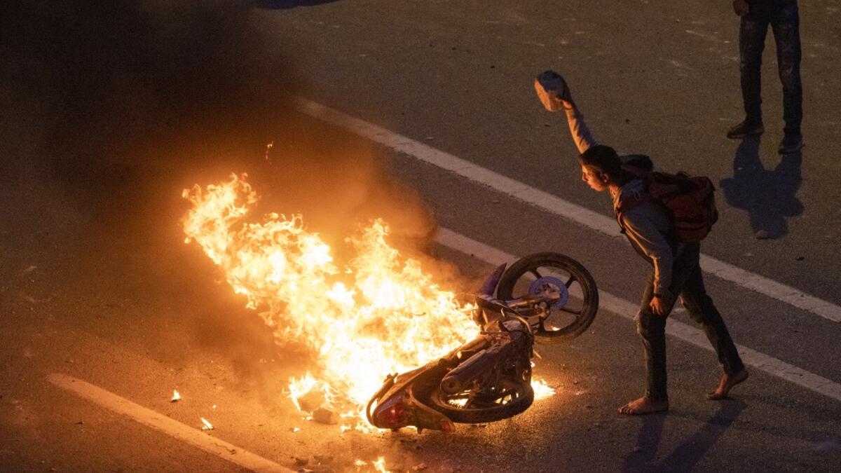 A migrant throws a rock onto a burning motorbike as they clash with Moroccan riot police in protest at being stopped from crossing the border, in the northern town of Fnideq, close to the border between Morocco and Spain's North African enclave of Ceuta on May 19, 2021. Migrants were still trying to cross from Morocco into the Spanish enclave of Ceuta on May 19, 2021, after a record 8,000 people poured over the border this week, escalating tensions between Rabat and Madrid