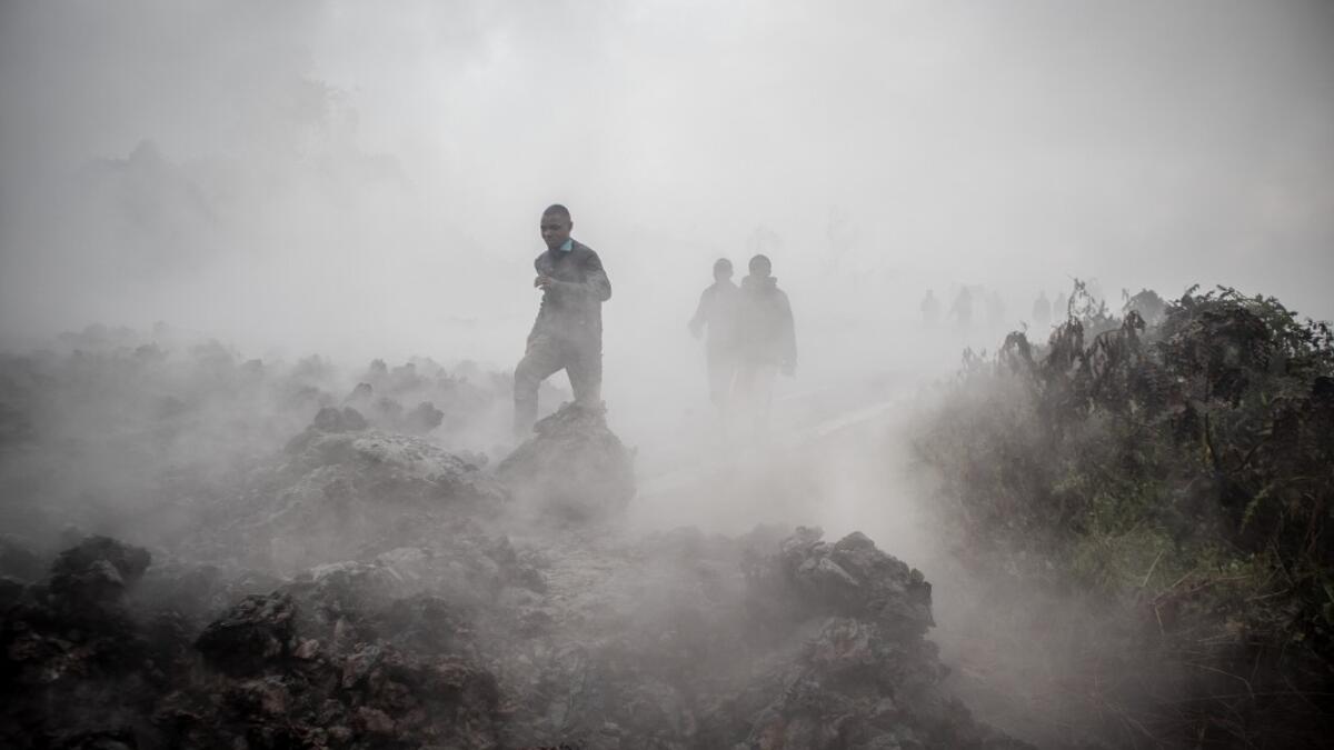 Men cross the front of the still smoking lava rocks from an eruption of the Mount Nyiragongo on May 23, 2021 in Goma in the East of the Democratic Republic of Congo. A river of boiling lava came to a halt on the outskirts of Goma Sunday, sparing the city in eastern DR Congo from disaster after the nighttime eruption of Mount Nyiragongo sent thousands of terrified residents fleeing in panic. Fire and strong fumes emanated from the blackish molten rock as it swallowed up houses