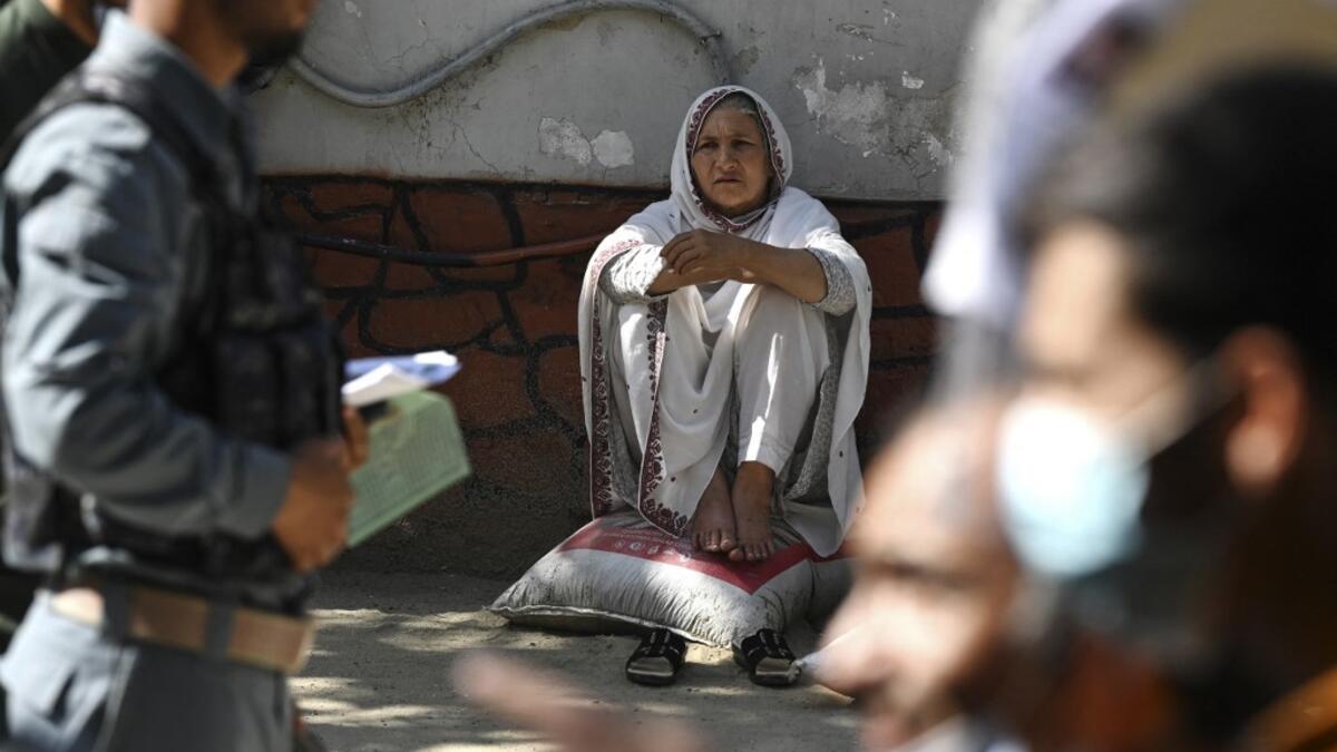 A woman sits as others queue to submit their passport applications at an office in Kabul on July 25, 2021. Dozens begin lining up at the passport office in Kabul before dawn most days, and by eight in the morning the queue already stretches for a good hundred metres.