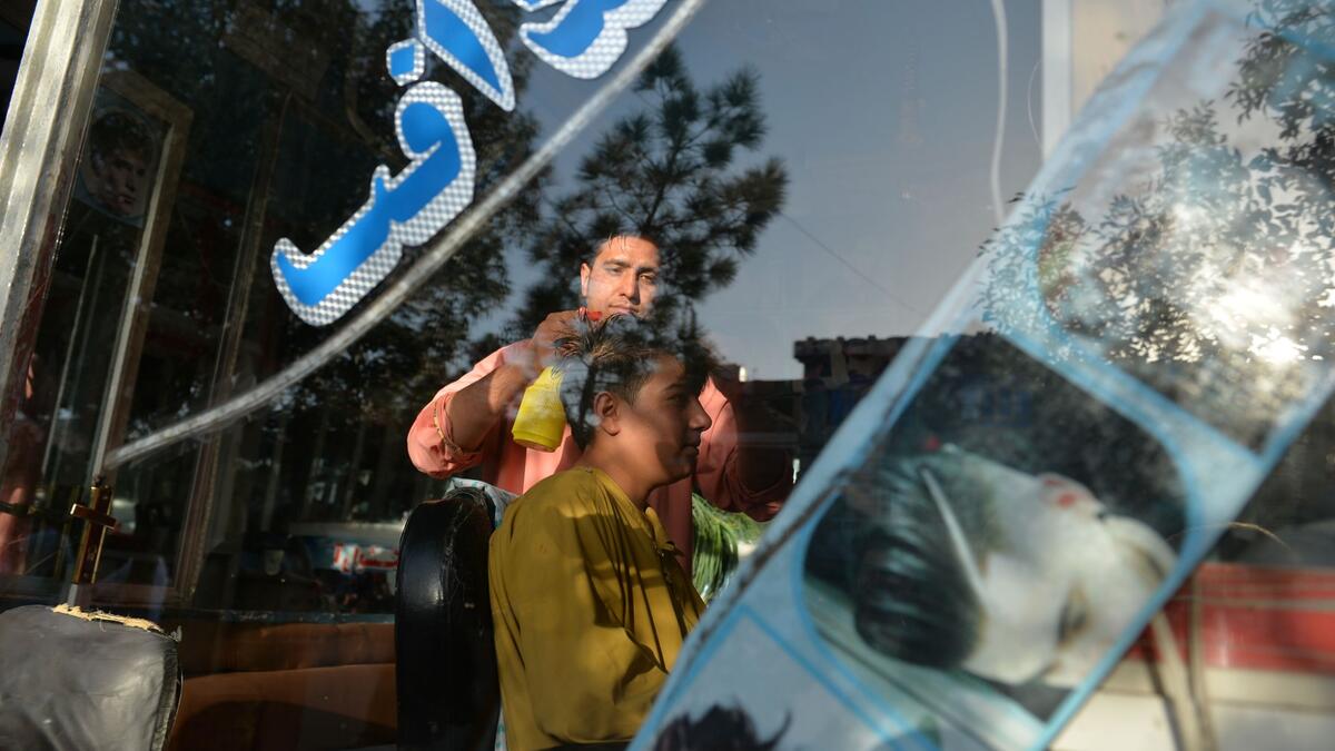 In this picture taken on September 19, 2021, 24-year-old Nader Shah (L) attends a customer at his barbershop in Herat. Quiffs, mohawks, and crew cuts were hairstyles Shah was accustomed to styling for image-conscious young men in Afghanistan’s third-biggest city of Herat.