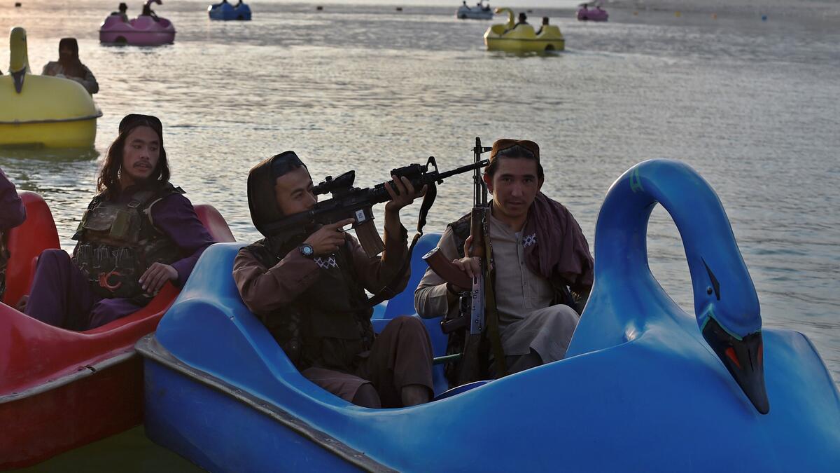 In this photograph taken on September 28, 2021 Taliban fighters ride on paddle boats at Qargha Lake on the outskirts of Kabul. "This is Afghanistan!" a Taliban fighter shouts on the pirate ship ride at a fairground in western Kabul, as his armed comrades cackle and whoop on board the rickety attraction. (Photo by WAKIL KOHSAR / AFP) / TO GO WITH: AFGHANISTAN-CONFLICT-FAIRGROUND, SCENE BY JAMES EDGAR - TO GO WITH: Afghanistan-conflict-fairground, SCENE by James EDGAR