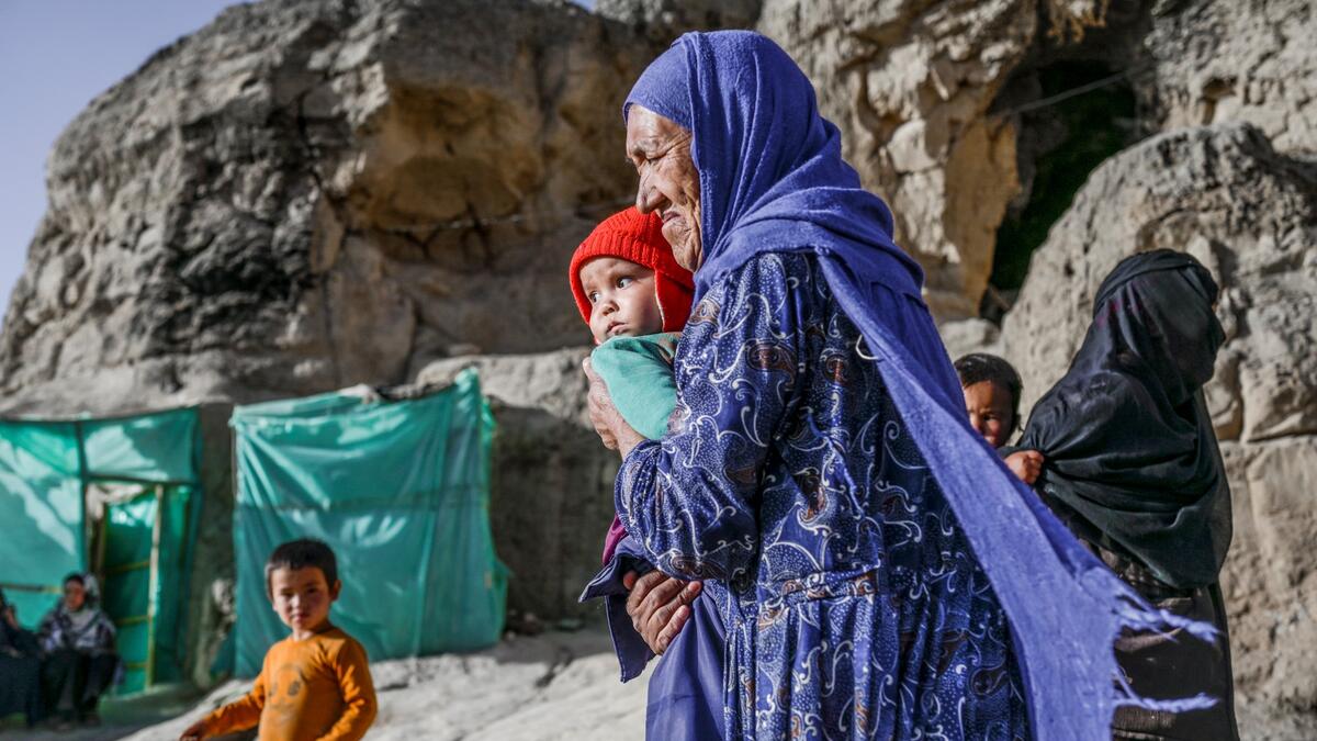 In this picture taken on October 3, 2021, a Hazara ethnic woman with a baby walks in front of her cave on a cliff pockmarked by caves where people still live as they did centuries ago in Bamiyan.