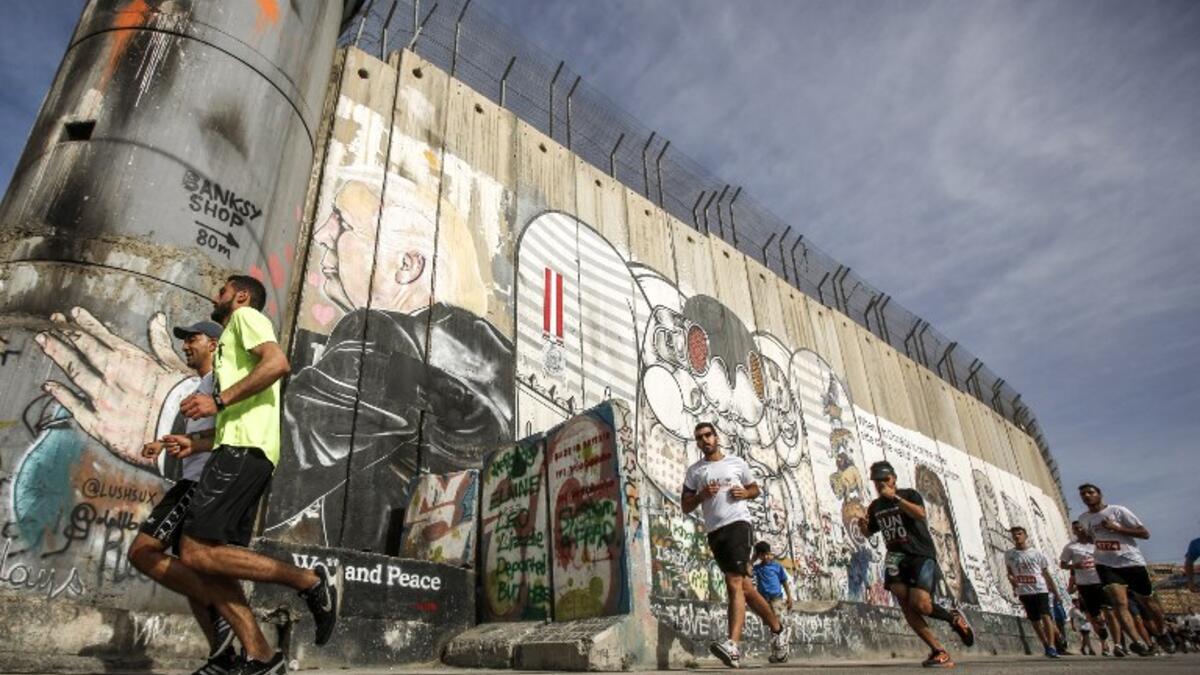 Participants run along Israel's controversial separation barrier, which divides the West Bank from Jerusalem, in the biblical town of Bethlehem during the 6th International Palestine Marathon on Mar. 23, 2018. 
(Musa AL SHAER / AFP)