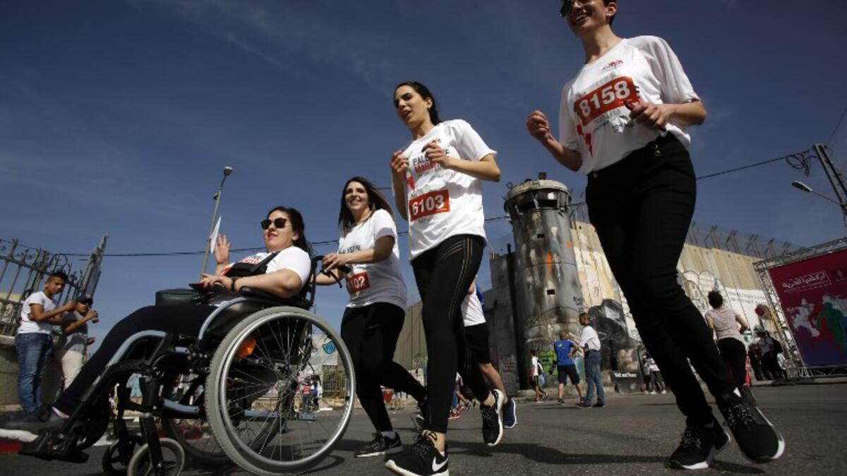 Participants push another in a wheelchair as they run along Israel's controversial separation barrier, which divides the West Bank from Jerusalem, in the biblical town of Bethlehem during the 6th International Palestine Marathon on Mar. 23, 2018. 
(Musa AL SHAER / AFP)