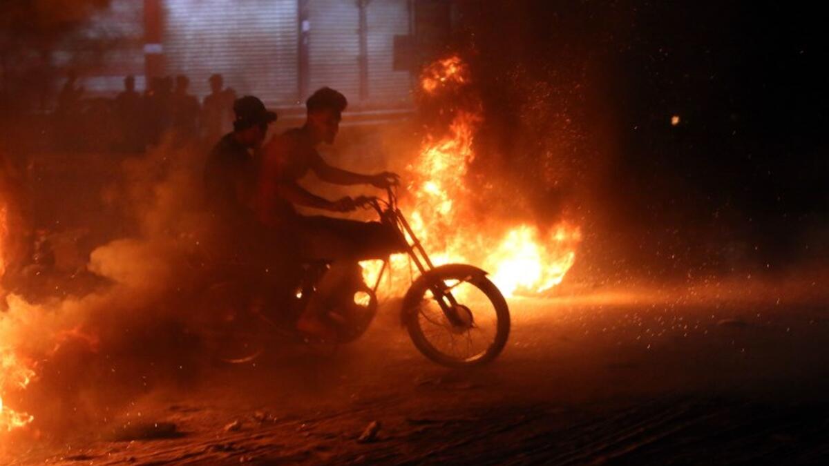 Demonstrators use a scooter to drive through burning tyres during an ongoing protest against unemployment and high cost of living in the southern Iraqi city of Basra during the night of July 12, 2018. (AFP/Haidar Mohammad Ali)