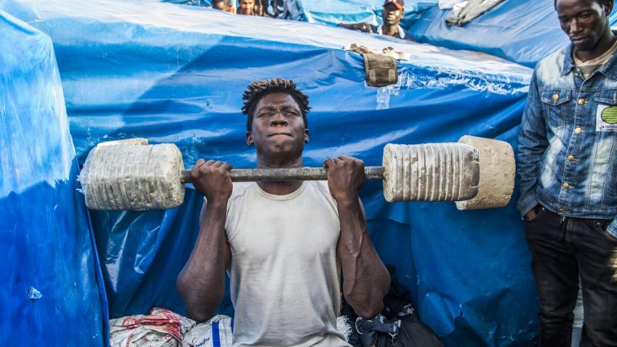 A sub-Saharan migrant lifts weights with a make-shift barbell between make-shift tents in the Oulad Ziane migrant camp in Casablanca on March 27, 2019. 
FADEL SENNA / AFP