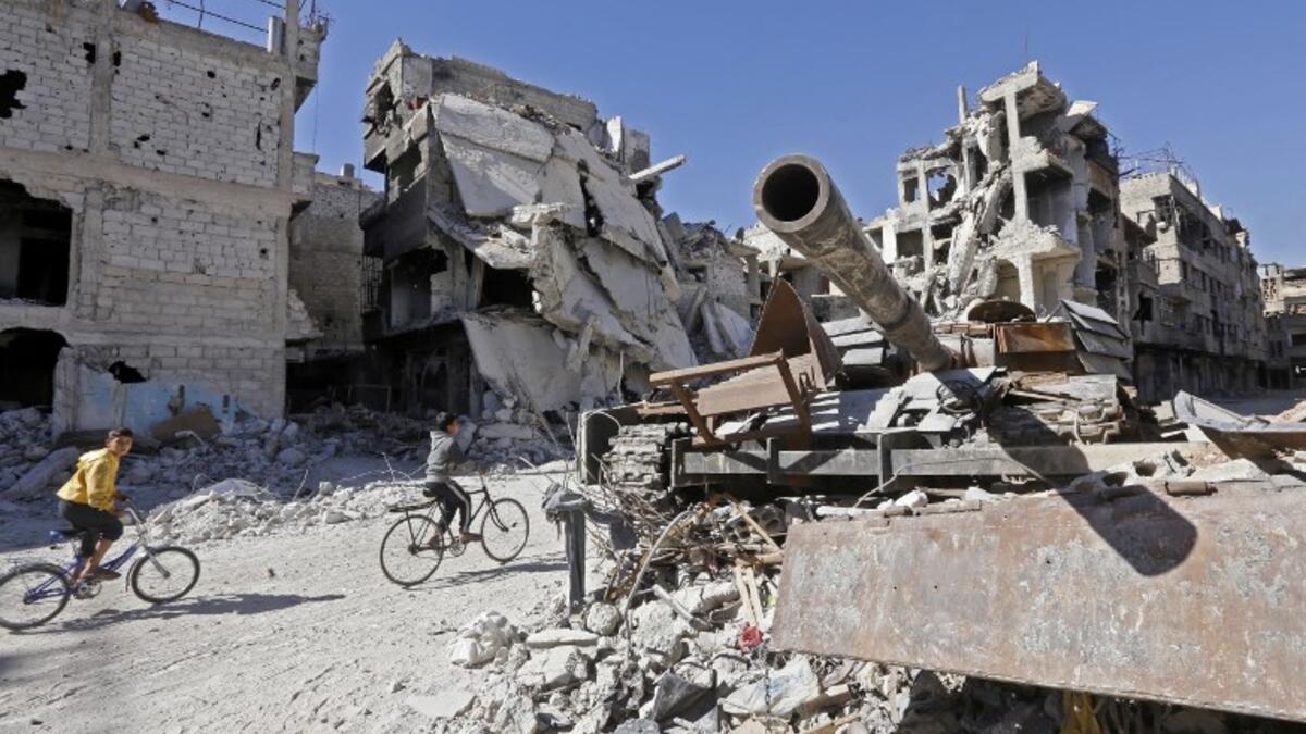 Boys ride their bicycle past a destroyed tank and buildings in the Palestinian camp of Yarmuk southern Damascus on November 1, 2018. 
LOUAI BESHARA / AFP