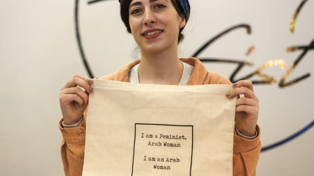 Amira Khader, Palestinian creative director of the feminist fashion label "BabyFist", poses with one of her canvas bags in her shop in Ramallah in the occupied West Bank 
ABBAS MOMANI / AFP