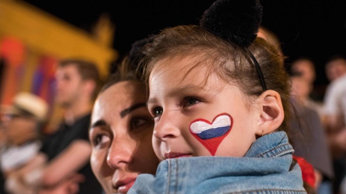 A woman holds a girl with a Russian flag shaped as a heart, painted on her left cheek as they watch the Russia 2018 World Cup Group D football match between Croatia and Nigeria on a giant screen at the official FIFA Fan Fest in Volgograd on June 16, 2018. 
NICOLAS ASFOURI / AFP