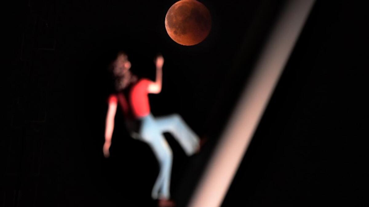 A "blood moon" eclipse is pictured with a sculpture by the American artist Jonathan Borofsky "Woman walking to the sky" on July 27, 2018 in Strasbourg, eastern France. (AFP/FREDERICK FLORIN)