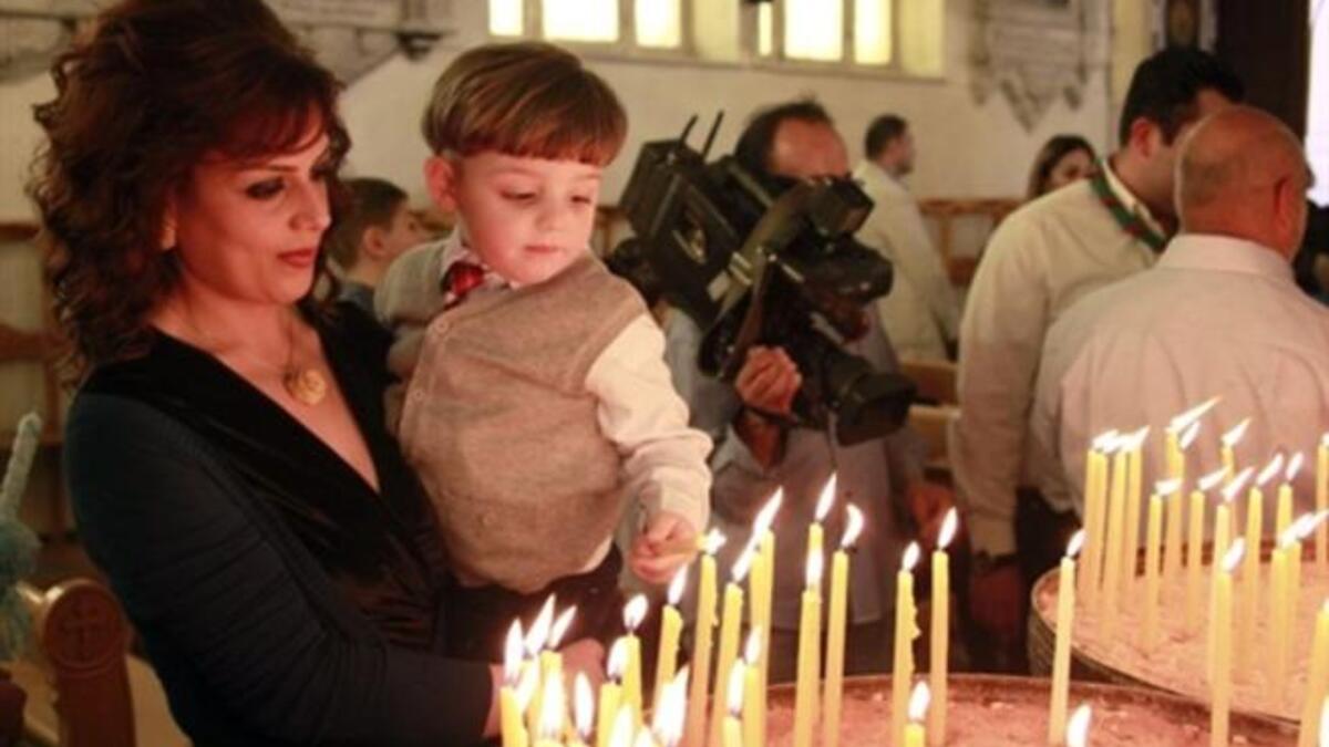 Syria's subdued celebrations in climate of unrest and fear still manage some cheering: A Christian Syrian woman holds her son as he lights a candle in Damascus while a cheering crowd waves palm leaves.