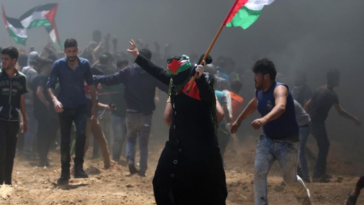 A Palestinian woman waves her national flag during clashes with Israeli forces near the border between Israel and the Gaza Strip, east of Jabalia on May 14, 2018, as Palestinians protest over the inauguration of the US embassy following its controversial move to Jerusalem. MOHAMMED ABED / AFP