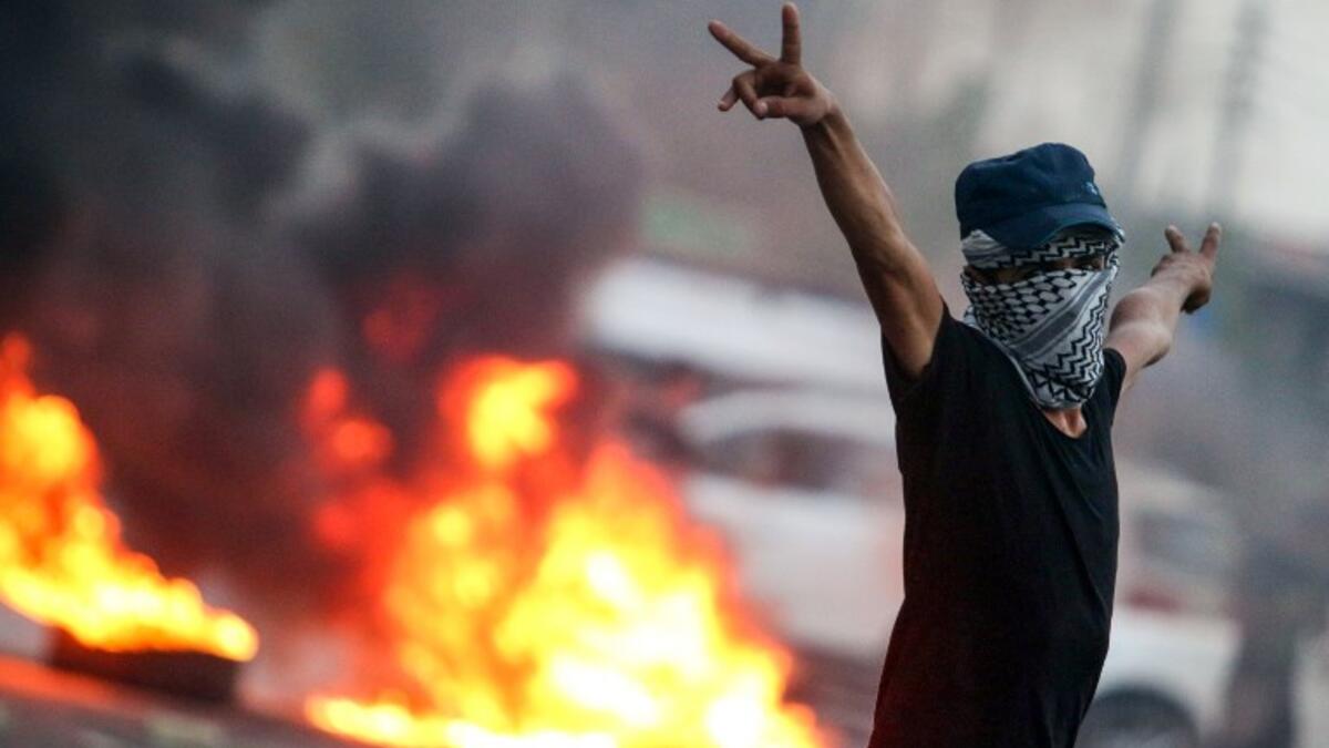 A masked Iraqi protester gestures while standing before burning tires during clashes with security forces in the southern city of Basra on September 2, 2018. 
Haidar MOHAMMED ALI / AFP
