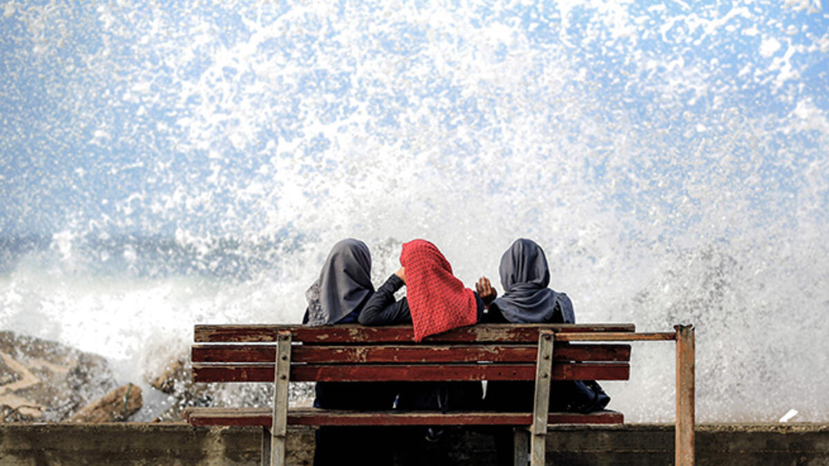 Three Palestinian women sit in the spray from the sea in Gaza City.