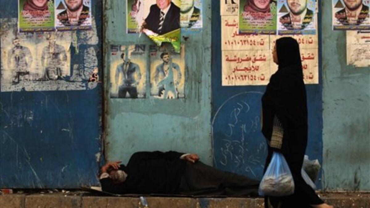 An Egyptian woman walks past a man sleeping next to a wall decorated with election campaign posters next to a polling station in Cairo, as the nation of some 41 million eligible voters goes to the polls.