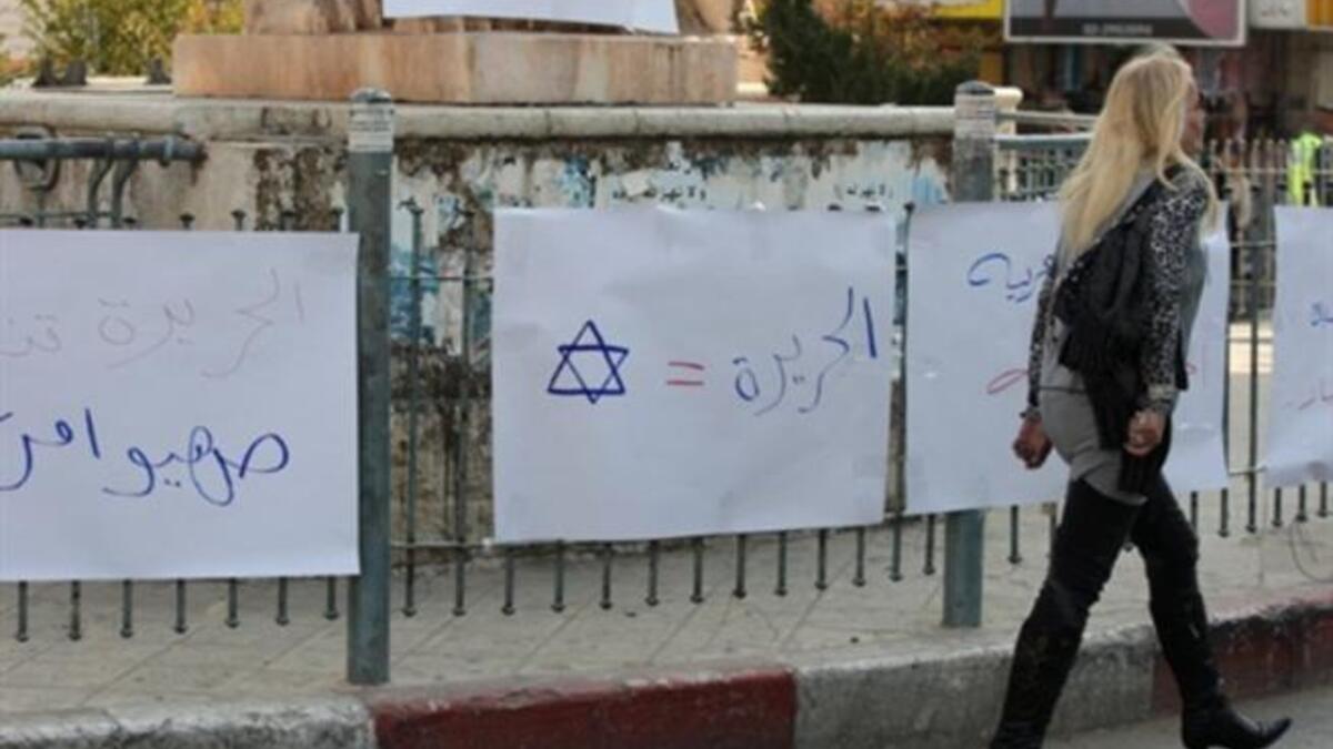 A Palestinian woman walks past placards denouncing Al-Jazeera during a protest near the offices of the pan-Arab news channel.