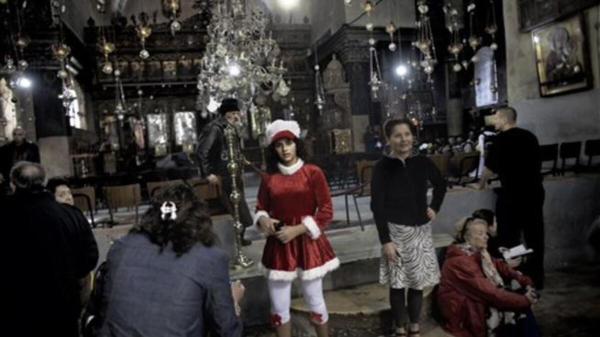 A Palestinian girl dressed in a Santa Claus attire poses alongside other worshippers inside the Church of the Nativity in the West Bank city of Bethlehem, as Christian flock to the what they believe is the birth place of Jesus Christ to celebrate his birth during Christmas mass.