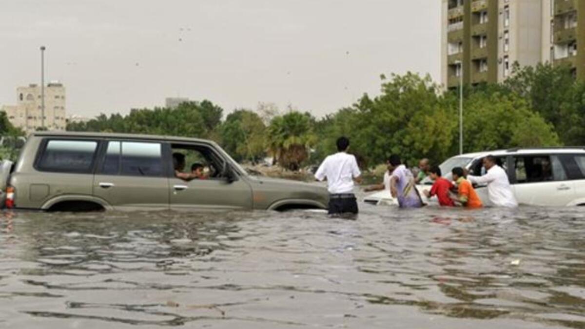 Saudi men are trying to push a car stuck in a flooded street.