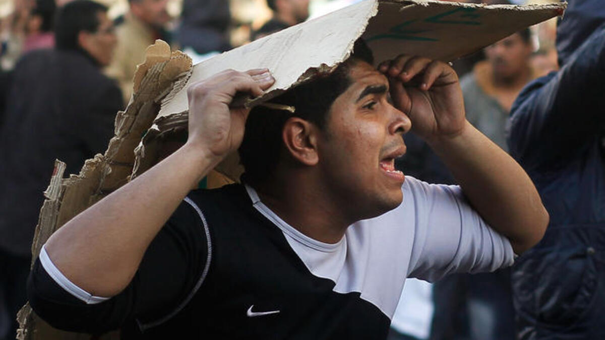 An opponent of embattled Egyptian president Hosni Mubarak tries to protect his head while calling for reinforcements during a clash between pro- and anti-Mubarak protesters.