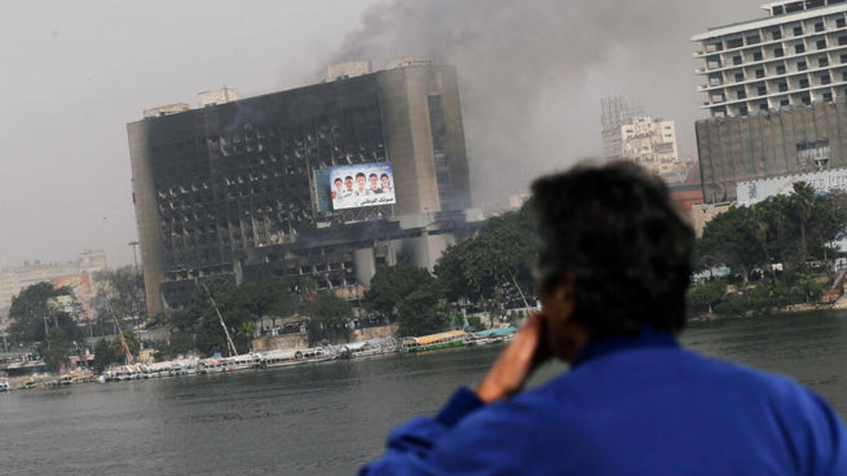 An Egyptian man looks out onto a burning government building from a bridge in central.