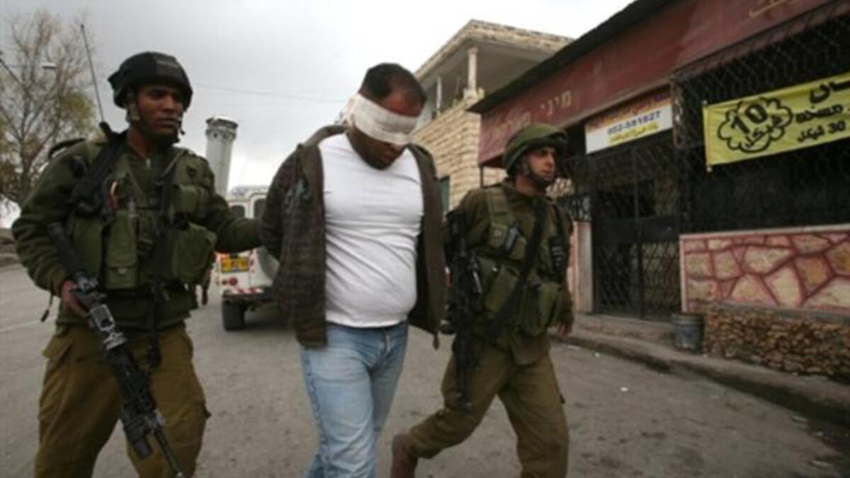 Israeli soldiers lead away a blind folded Palestinian man during a military operation at the entrance of the village of Beit Omar village in the Israeli occupied West Bank.