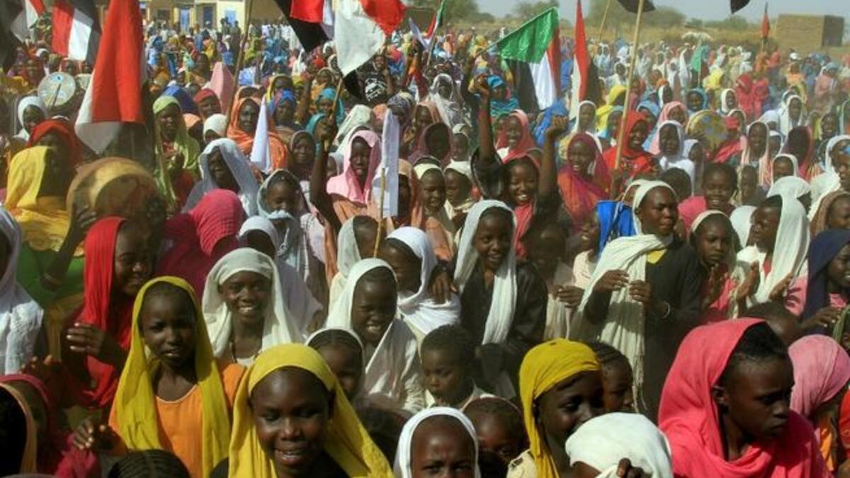 Sudanese women wave their national flag as they wait for the arrival of special envoys in the Shangil Tobaya area for displaced people in North Darfur state (AFP)