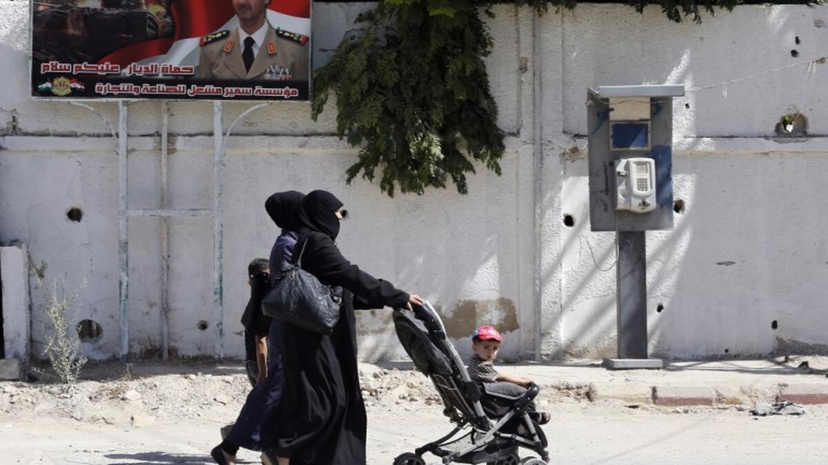 Women walks past a poster of Syrian President Bashar al-Assad during Syria's first local elections since 2011, on September 16, 2018. (LOUAI BESHARA / AFP)