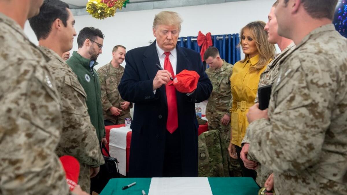 US President Donald Trump signs a hat as First Lady Melania Trump looks on as they greet members of the US military during an unannounced trip to Al Asad Air Base in Iraq on December 26, 2018. President Donald Trump arrived in Iraq on his first visit to US troops deployed in a war zone since his election two years ago. SAUL LOEB / AFP