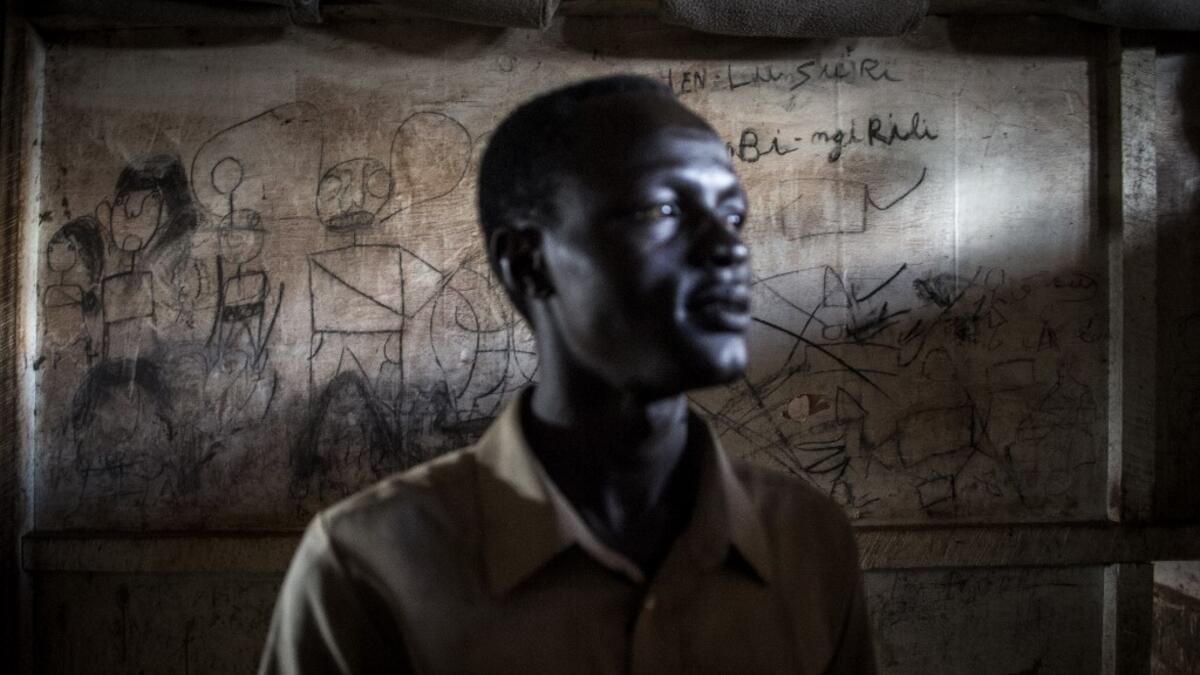 John Aremic, 20, a South Sudanese Refugee stands in front of a wall filled with drawings and writings depicting scenes from home in a building located in a transition camp for South Sudanese refugees who have just arrived in Aru. JOHN WESSELS / AFP