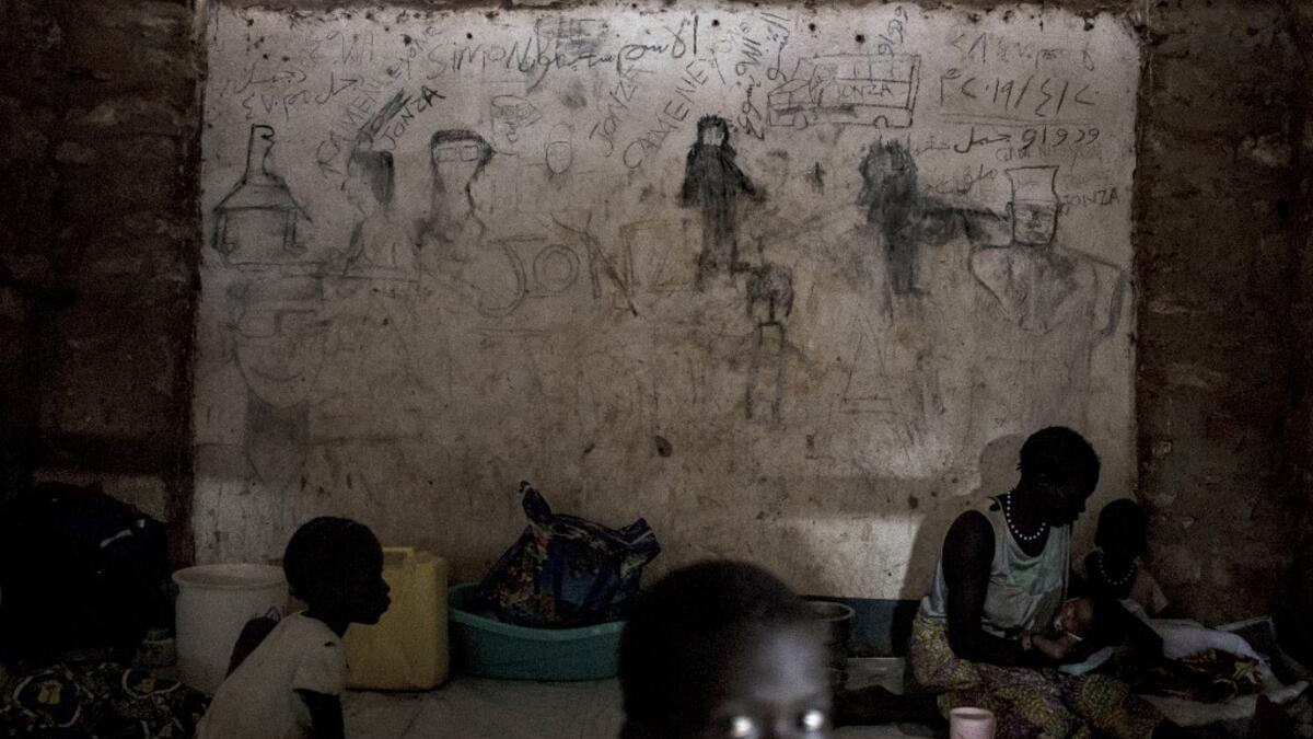 South Sudanese refugees sit in front of a wall filled with drawings and writings depicting scenes from home in Aru JOHN WESSELS / AFP