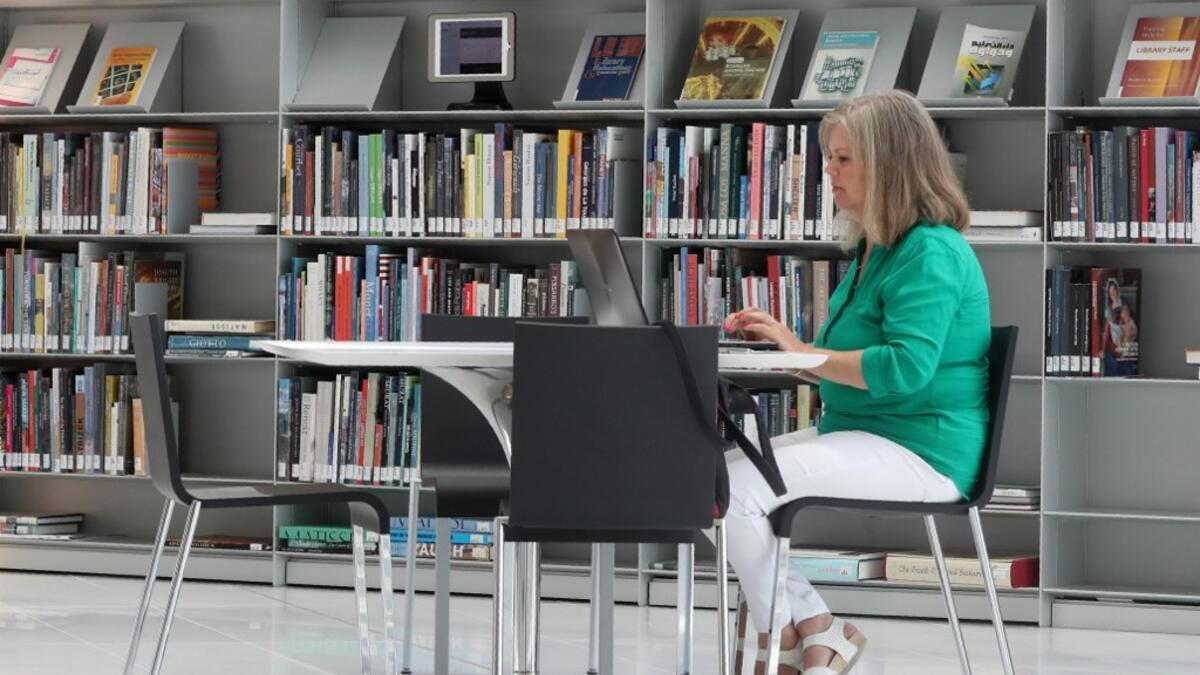A woman works on a latpop at a table inside the Qatar National Library in the capital Doha.  KARIM JAAFAR / AFP