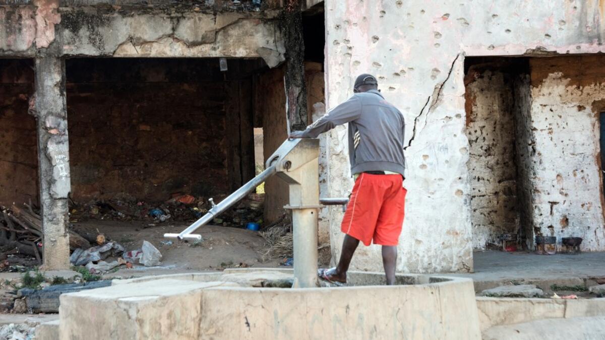 A man uses a hand pump to wash his feet outside a building damaged by bullet holes, dating from the Angolan civil war RODGER BOSCH / AFP