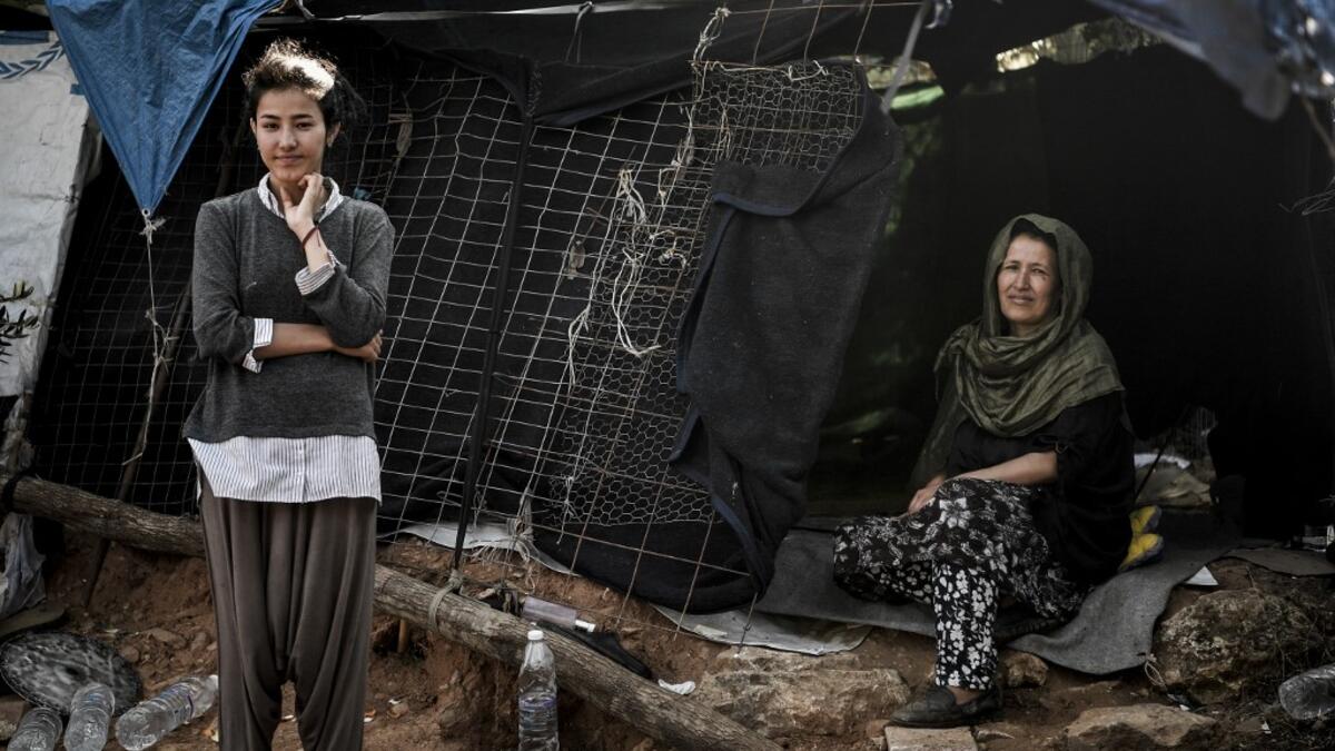A mother and daughter pose in front of their makeshift shelter at the Samos refugee camp, just above the island's capital city of Vathy.  LOUISA GOULIAMAKI / AFP