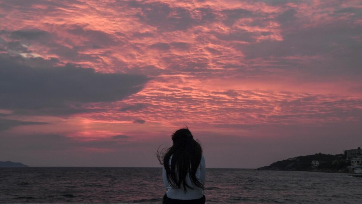 A young migrant girl watches the sunset at the city of Vathy on the island of Samos early.   LOUISA GOULIAMAKI / AFP