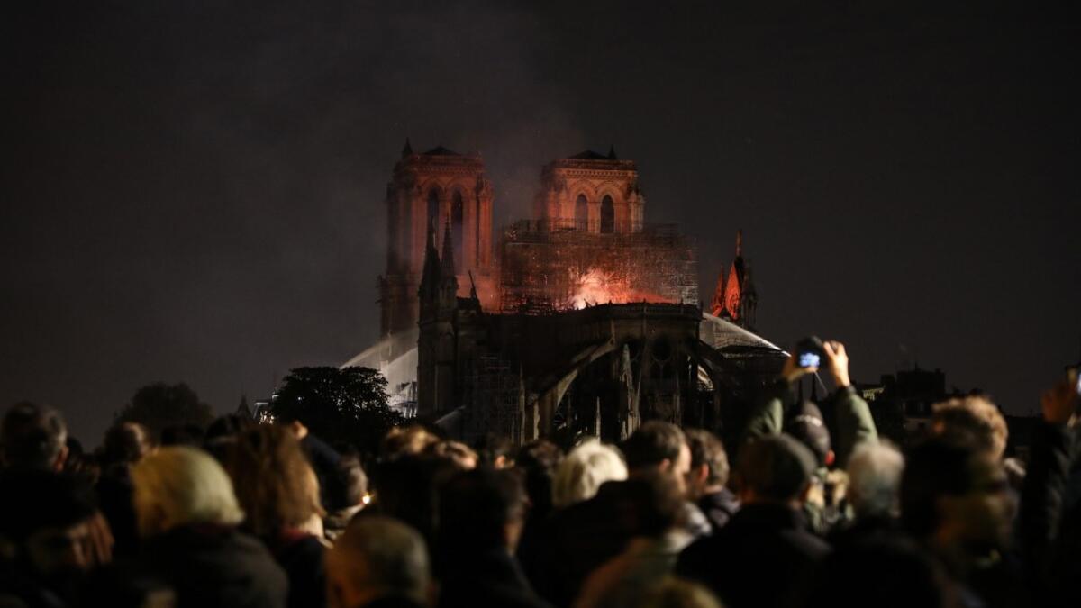 People watch as Notre-Dame de Paris Cathedral burns late into the night on April 15, 2019, in the French capital Paris.  A huge fire swept through the roof of the famed Notre-Dame Cathedral in central Paris on April 15, 2019. ludovic MARIN / AFP