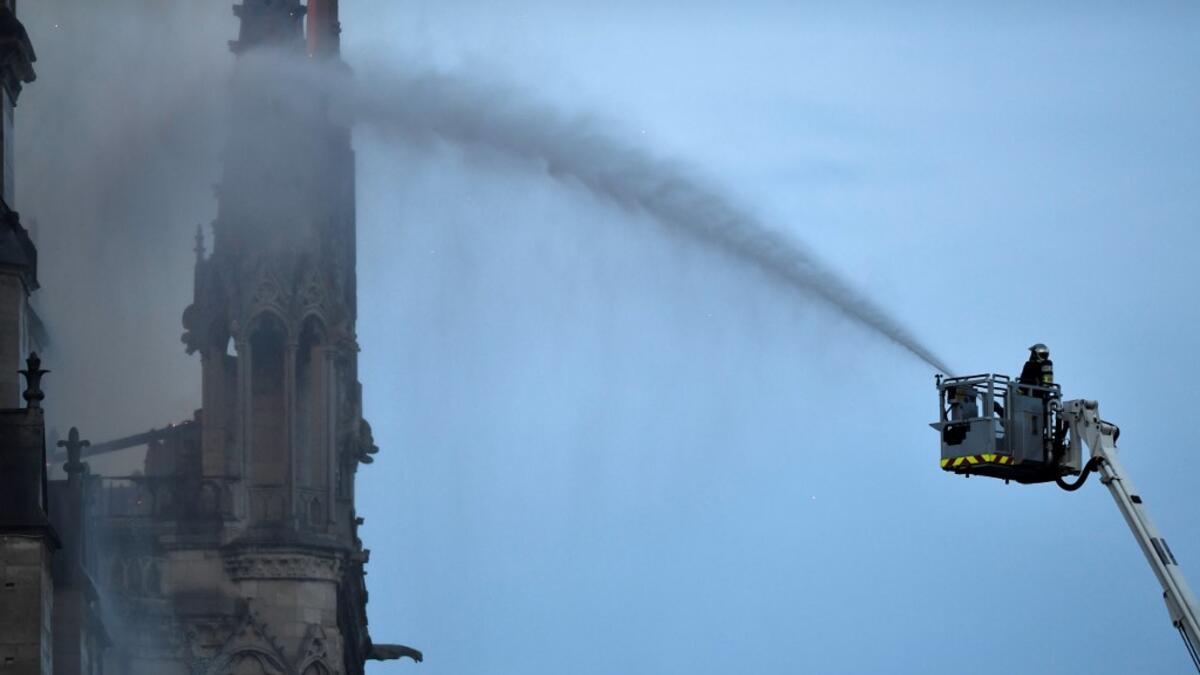 A Firefighter douse flames billowing from the roof at Notre-Dame Cathedral in Paris on April 15, 2019. A major fire broke out at the landmark Notre-Dame Cathedral in central Paris sending flames and huge clouds of grey smoke billowing into the sky. FRANCOIS GUILLOT / AFP