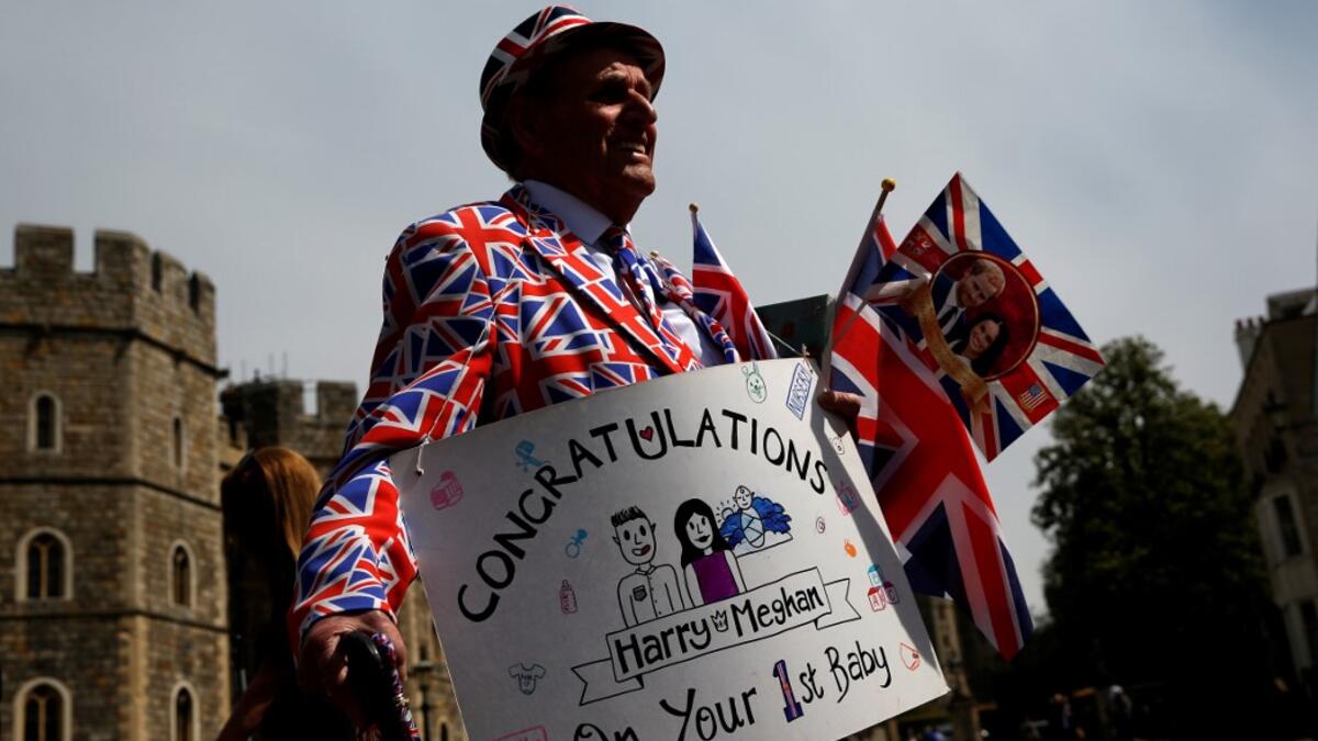 Royal super fan Terry Hutt, wearing a Union-flag themed suit, holds a congratulatory banner as he walks outside Windsor Castle in Windsor, west of London on May 7, 2019, the day after the announcement that Britain's Meghan, Duchess of Sussex had given birth to a son. ADRIAN DENNIS / AFP